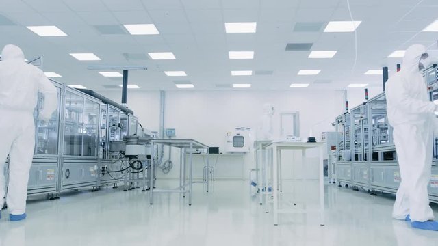 Team of Research Scientists in Sterile Suits Working with Computers, Microscopes and Modern Industrial Machinery in the Laboratory. Shot on RED EPIC-W 8K.