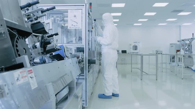 In the Laboratory Scientist Wearing Sterile Protective Coverall Set's up / Programs Modern Industrial 3D Printer, High Precision Manufacture of Semiconductors under Process.
