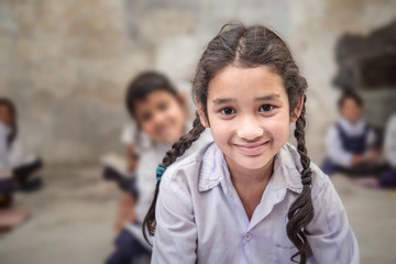  School girl in uniform of Indian Ethnicity sitting in their village classroom, looking at camera smiling.