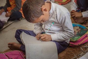 Concentrated Rural school kid studying on floor and writing in the notebook