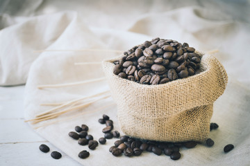 Fototapeta na wymiar Coffee beans in burlap sack and stick on white wood background