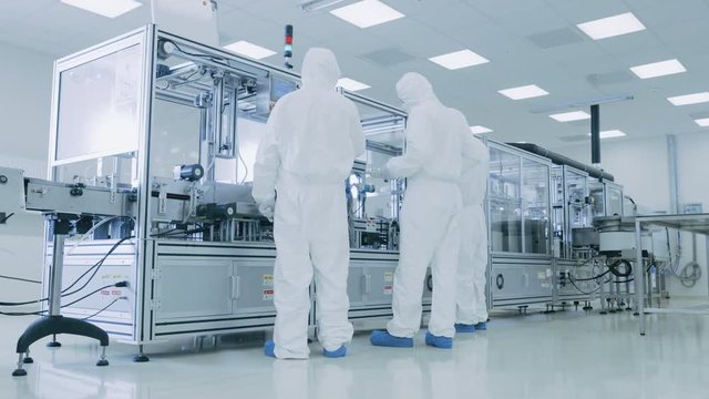 In the Manufacturing Facility Team of Scientist Wearing Sterile Protective Coverall Set up / Program Modern Industrial 3D Printer, High Precision Manufacture of Semiconductors under Process.
