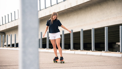 Young Beautiful Blonde Girl Riding Bright Skateboard on the Bridge