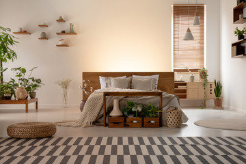 Real photo of an eco bedroom interior with a double bed, striped carpet, plants, lamps and empty...
