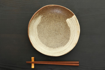 黒いテーブルに置かれた土製の皿と箸