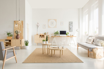 Wooden table on brown carpet between sofa and armchair in white open space interior. Real photo