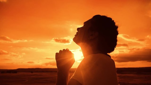 the girl prays. Girl folded her hands in prayer silhouette at sunset lifestyle. slow motion video. Girl folded her hands in prayer pray to God. girl praying asks forgiveness for sins of repentance
