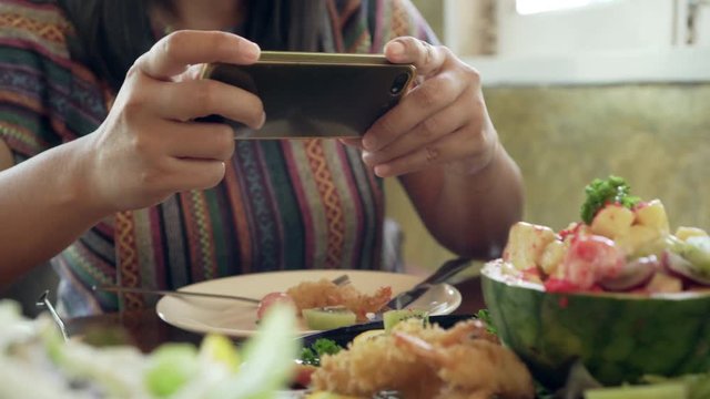 Attractive asian woman taking picture of a fruit salad on her smart phone at a table. Close up. 4K.