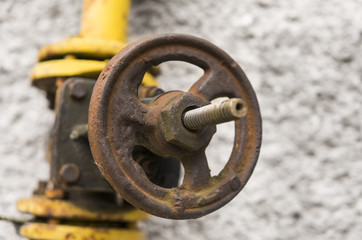 Old weathered gas crane and pipe on the background of a gray wall. Old gas gate of yellow colour is...