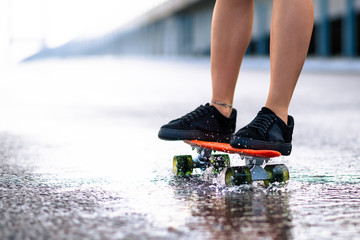 Close up of Woman Legs Riding Orange Skateboard on the Wet Road in the Rain