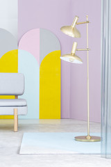 Real photo of a golden floor lamp and a gray sofa in colorful living room interior with geometric...