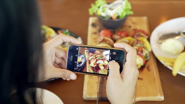 Attractive asian woman taking picture of a fruit salad on her smart phone at a table. Close up. 4K.