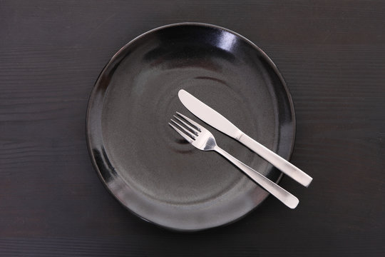 黒い木製テーブルに置かれた黒い皿とカトラリーによる食事終了の合図