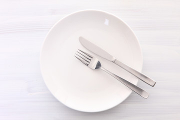 白い木製テーブルに置かれた白い皿とカトラリーによる食事終了の合図