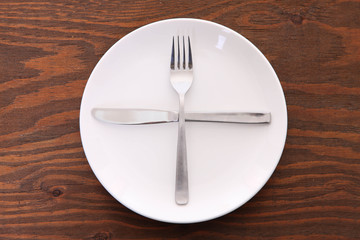 茶色い木製テーブルに置かれた白い皿とカトラリーによる次の料理を待機の合図