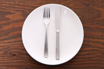 
茶色い木製テーブルに置かれた白い皿とカトラリーによる食事終了のサイン
