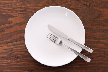 
茶色い木製テーブルに置かれた白い皿とカトラリーによる食事終了のサイン
