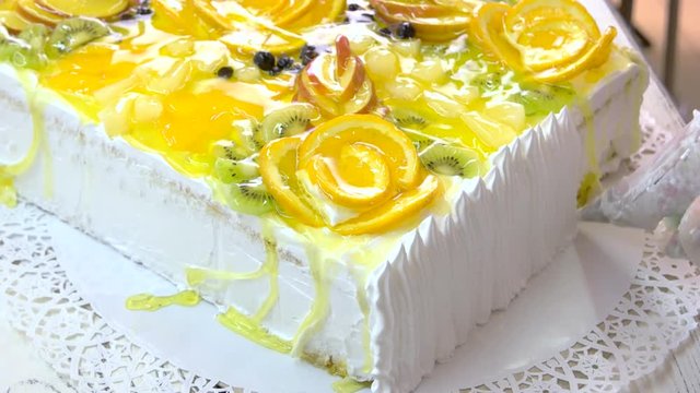 Chef decorating cake with white cream. Cake covered with fresh fruits slices and jelly. Delicious dessert for gourmet.