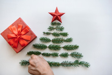 Creative idea for Christmas or New Year theme. A person makes a creative Christmas or New Year tree from fir branches and a star on top. There is a gift to the red box next to it.
