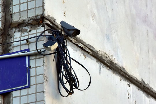 CCTV camera on the concrete wall of house. a long cable coil is next to it. poor-quality installation. lack of stealth