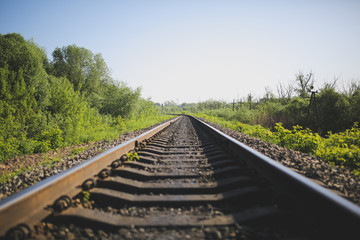 Obraz premium Rail tracks in the green field. Railway transport industry. Empty road on summer day. Travel lifestyle motivation photo.