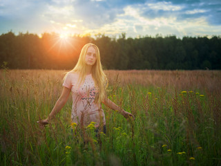 Fototapeta na wymiar Cute blonde woman posing on sunset on flowering meadow field