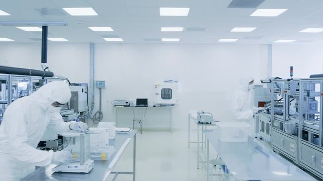 Quality Control Check: Scientist Using Digital Tablet Computer and wearing Protective Suit walks through Manufacturing Laboratory. Product Manufacturing: Pharmaceutics, Semiconductors, Biotechnology.