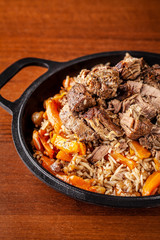 Traditional Uzbek oriental cuisine, pilaf or plov with large pieces of lamb meat and carrots, cooked in a black cast-iron skillet of kazan. Copy space, selective focus