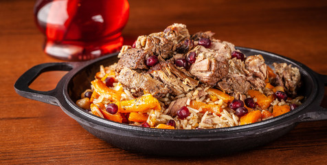 Traditional Uzbek oriental cuisine, pilaf or plov with large pieces of lamb meat and carrots, cooked in a black cast-iron skillet of kazan. Copy space, selective focus