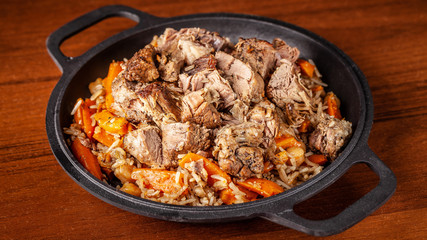 Traditional Uzbek oriental cuisine, pilaf or plov with large pieces of lamb meat and carrots, cooked in a black cast-iron skillet of kazan. Copy space, selective focus