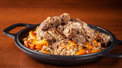 Traditional Uzbek oriental cuisine, pilaf or plov with large pieces of lamb meat and carrots, cooked in a black cast-iron skillet of kazan. Copy space, selective focus