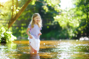 Cute little girl playing by a river on hot summer day. Adorable child having fun outdoors during summer vacations.