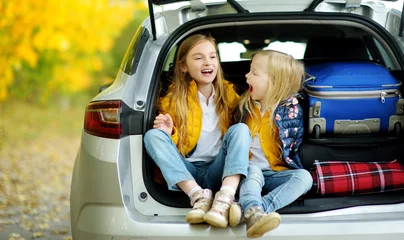 Fotobehang Two adorable girls sitting in a car trunk before going on vacations with their parents. Two kids looking forward for a road trip or travel. Autumn break at school. © MNStudio