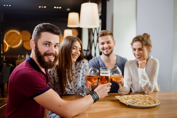 Man holding glass of beer and sitting in pizzeria with friends.