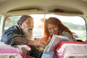 Old hipster couple sitting in a car and looking at a road map 