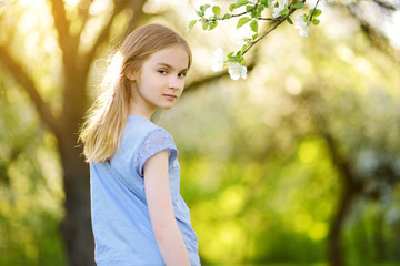 Adorable preteen girl in blooming apple tree garden on beautiful spring day