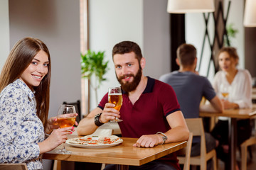Beautiful couple holding glasses of wine and beer in pizzeria.
