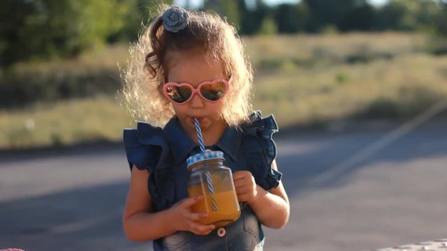 Child girl in sunglasses drinks smoothies in the rays of sunset on a summer day. Close up
