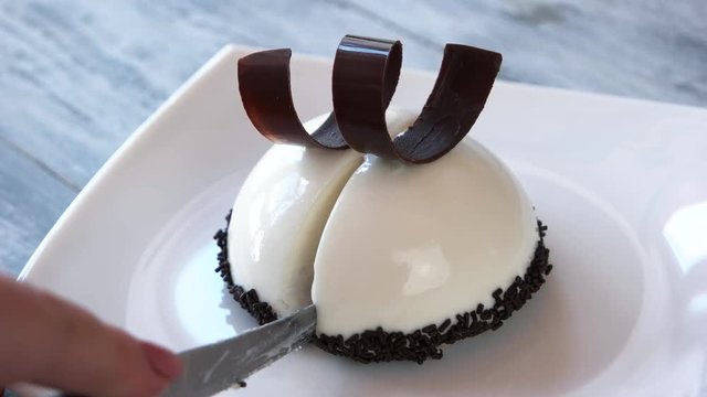 Mousse hemispherical cake with vanilla flavor. Cutting of dome shaped dessert in two pieces. Yummy pastry at restaurant.