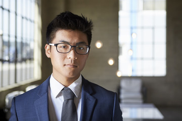 Young Asian businessman looking to camera, head and shoulders