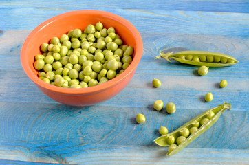 peas in an orange Cup and pea pods on a blue background