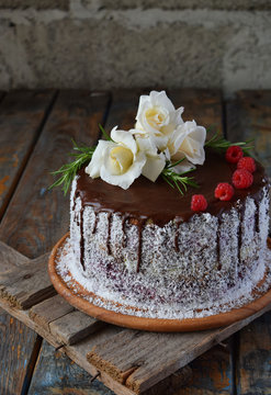 Gluten-free and dairy-free cake decorated with white roses and coconut: chocolate-nut biscuit, berry mousse, custard on almond milk and chocolate glaze. Healthy dietary baking. Vegetarian food.