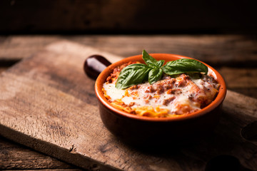 Traditional lasagne in a casserole dish on wooden table - obrazy, fototapety, plakaty