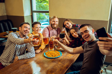 people, leisure, friendship and communication concept - happy friends drinking beer, talking and clinking glasses at bar or pub