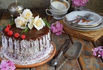 Fototapeta na wymiar Gluten-free and dairy-free cake decorated with white roses and coconut: chocolate-nut biscuit, berry mousse, custard on almond milk and chocolate glaze. Healthy dietary baking. Vegetarian food.