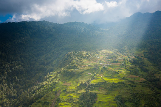 Terraced fields on a Himalayan hillside with rays of sunlight streaming down lighting up the village.