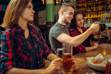 people, leisure, friendship and communication concept - happy friends drinking beer, talking and clinking glasses at bar or pub