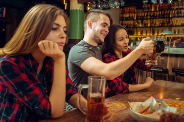 people, leisure, friendship and communication concept - happy friends drinking beer, talking and clinking glasses at bar or pub