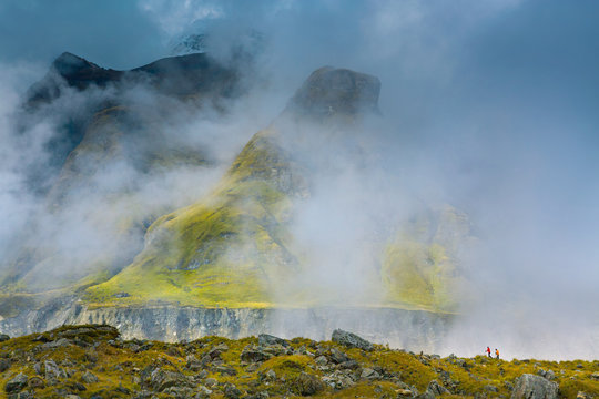 Two hikers trekking on a ridge in the fog above the glacial moraine at Annapurna Base Camp in the Himalaya of Nepal.