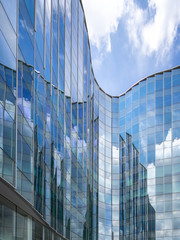 Modern glass building with reflection of blue sky and clouds.